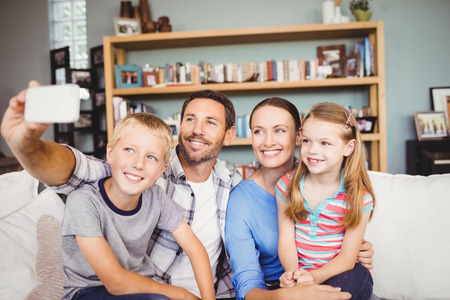 Happy family taking selfie with mobile phone while sitting on sofa at homeの写真素材