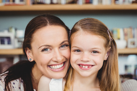 Close-up portrait of cheerful mother embracing daughter at home
