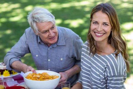 Senior man offering crisps to young woman in a parkの写真素材