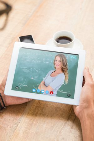 Smiling teacher standing arms crossed in front of blackboard against woman holding tablet computer with blank screenの写真素材