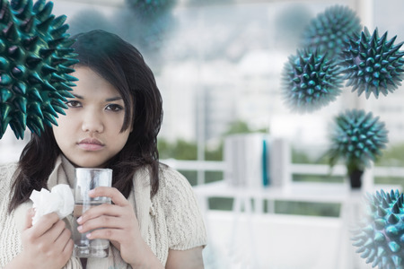 Sick woman holding a tissue and a glass of water against office