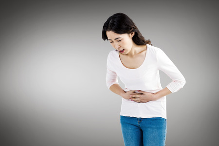 Young woman with stomach pain against white screenの写真素材