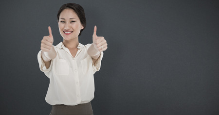 Business colleagues gesturing thumbs up in office against grey backgroundの写真素材
