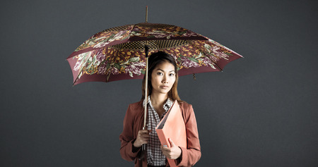Businesswoman with an umbrella holding a binder against grey backgroundの写真素材