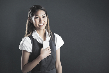 Smiling businesswoman holding a smartphone against grey backgroundの写真素材