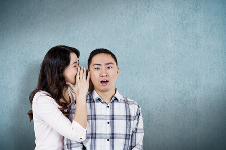 Woman whispering secret to husband  against blue backgroundの写真素材