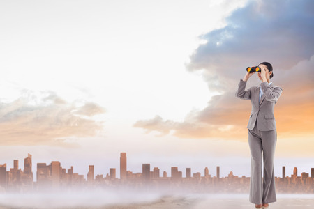 Portrait of a brunette businesswoman looking through binoculars against sandy path leading to large urban cityの写真素材