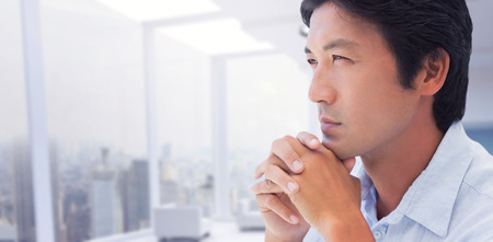 Thinking man with hands together against modern room overlooking cityの写真素材