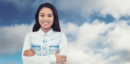 Asian woman with arms crossed smiling against blue sky with cloudsの写真素材