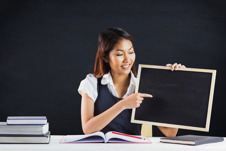 Smiling businesswoman pointing a blackboard against black backgroundの写真素材