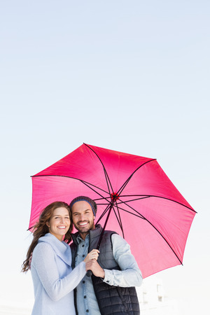 Portrait of happy young couple holding pink umbrella togetherの写真素材
