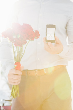 Happy young man holding engagement ring and flower bouquetの写真素材
