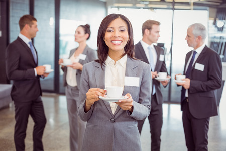 Portrait of businesswoman having tea during break time and her team interacting in background