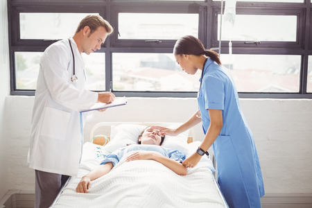 Doctor and a nurse stand around a patients bed as they are examining him in hospitalの写真素材