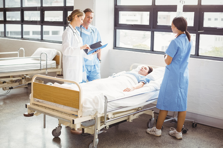 Doctor and a nurse stand around a patients bed as they are examining him in hospitalの写真素材