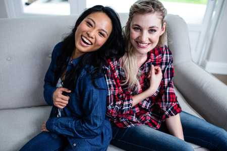 Portrait of happy young beautiful friends sitting on sofa at homeの写真素材