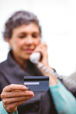 Close-up of mature woman holding payment card while talking on telephone at homeの写真素材