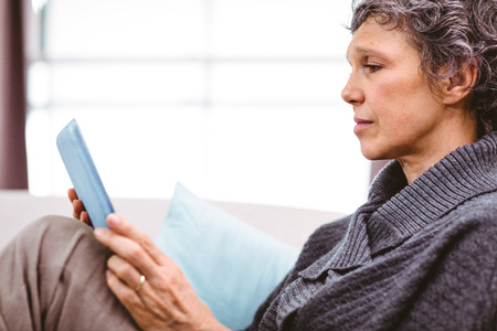 Close-up of mature woman using digital tablet while siting on sofa at homeの写真素材