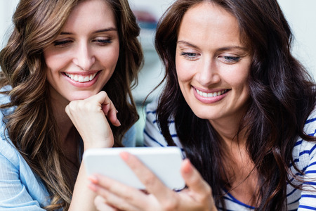 Close-up of cheerful female friends using mobile phone at homeの写真素材
