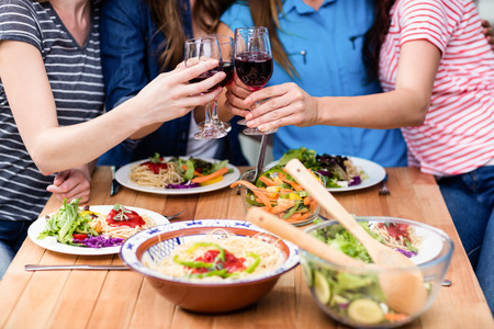 Midsection of friends toasting red wine glasses at tableの写真素材