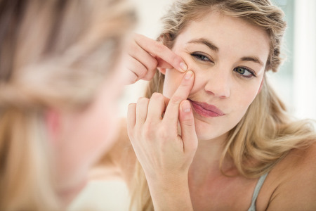 Concerned young woman looking in mirror while standing at homeの写真素材