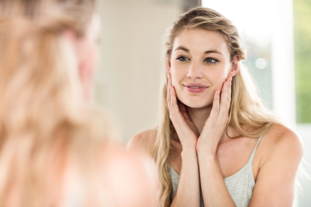Happy young woman looking in mirror at homeの写真素材