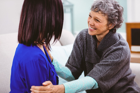 Happy mother talking to daughter sitting on sofa at home