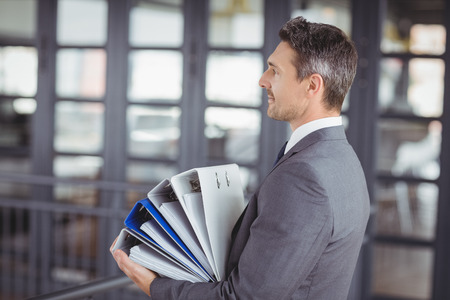 Side view of businessman carrying files stack in officeの写真素材