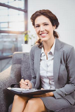 Portrait of happy businesswoman with diary sitting on sofa at officeの写真素材