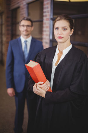 Portrait of confident female lawyer with businessman standing in background at officeの写真素材