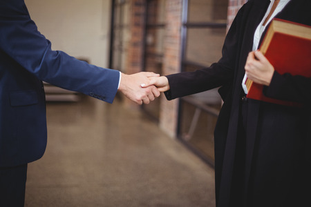Midsection of female lawyer handshaking with client while standing in officeの写真素材