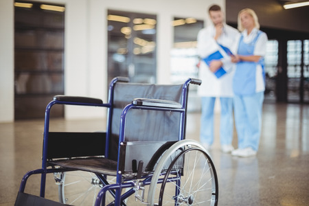 Empty wheelchair with colleagues discussing on backgroundの写真素材