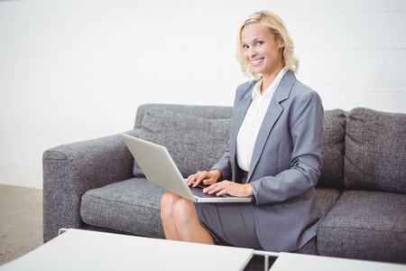 Portrait of smiling bussinesswoman working on laptop while sitting on sofa at officeの写真素材