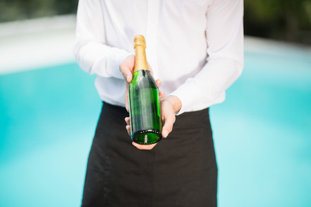 Midsection of waiter holding champagne bottle at poolsideの写真素材