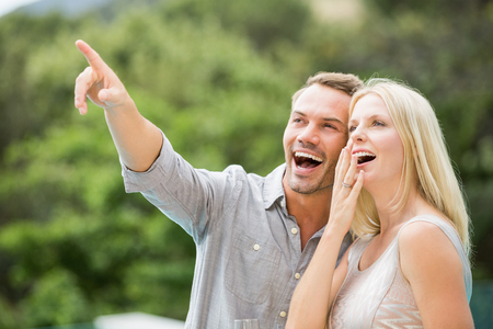 Smiling man pointing while standing by surprised woman at resortの写真素材
