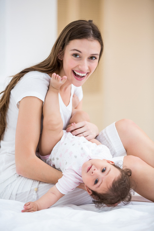 Portrait of smiling mother holding baby on bed at homeの写真素材