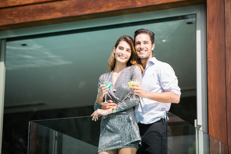 Happy couple with drinks standing in balcony at resortの写真素材