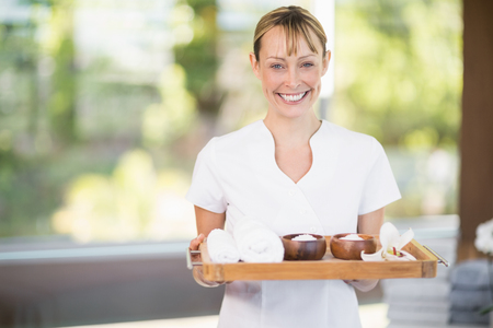 Portrait of female masseur smiling while holding tray with spa therapy productsの写真素材