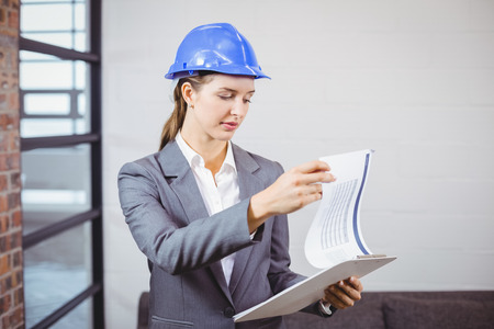 Female architect checking documents while standing in buildingの写真素材