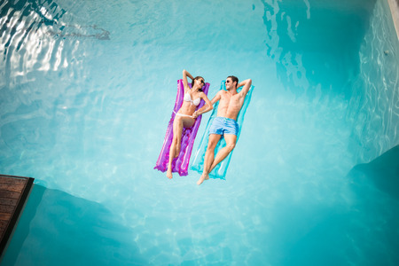High angle view of happy couple relaxing on inflatable raft at swimming pool