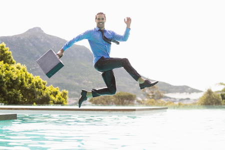 Happy businessman with briefcase jumping over swimming poolの写真素材