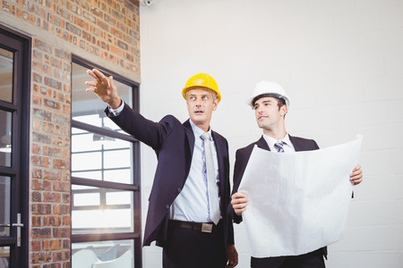 Male architect with colleague holding blueprint in buildingの写真素材