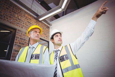 Architect pointing with colleague holding blueprint in building