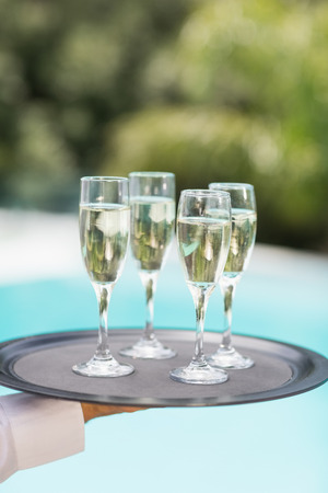 Cropped hands of waiter holding champagne flutes tray at poolsideの写真素材