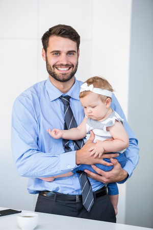 Portrait of cheerful businessman carrying daughter by table at homeの写真素材