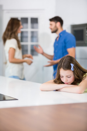 Upset girl leaning on table against parents at homeの写真素材