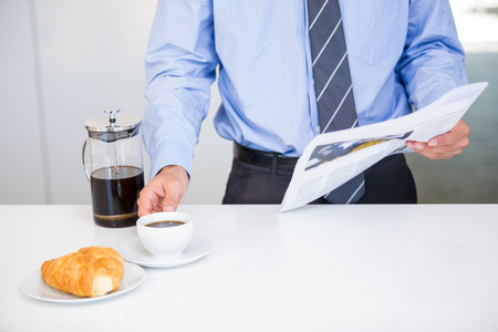 Midsection of businessman holding coffee cup and newspaper while standing by tableの写真素材