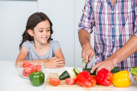Midsection of father cutting vegetables with daughter at homeの写真素材