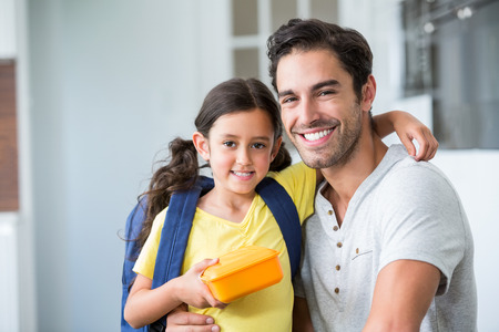 Portrait of smiling father and daughter with lunch box at homeの写真素材