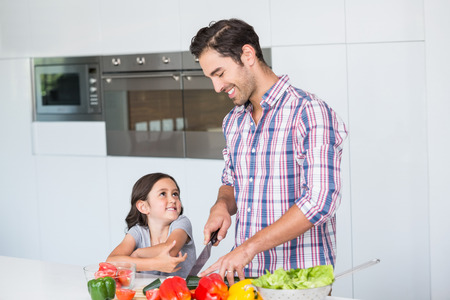 Smiling father cutting vegetables with daughter at homeの写真素材